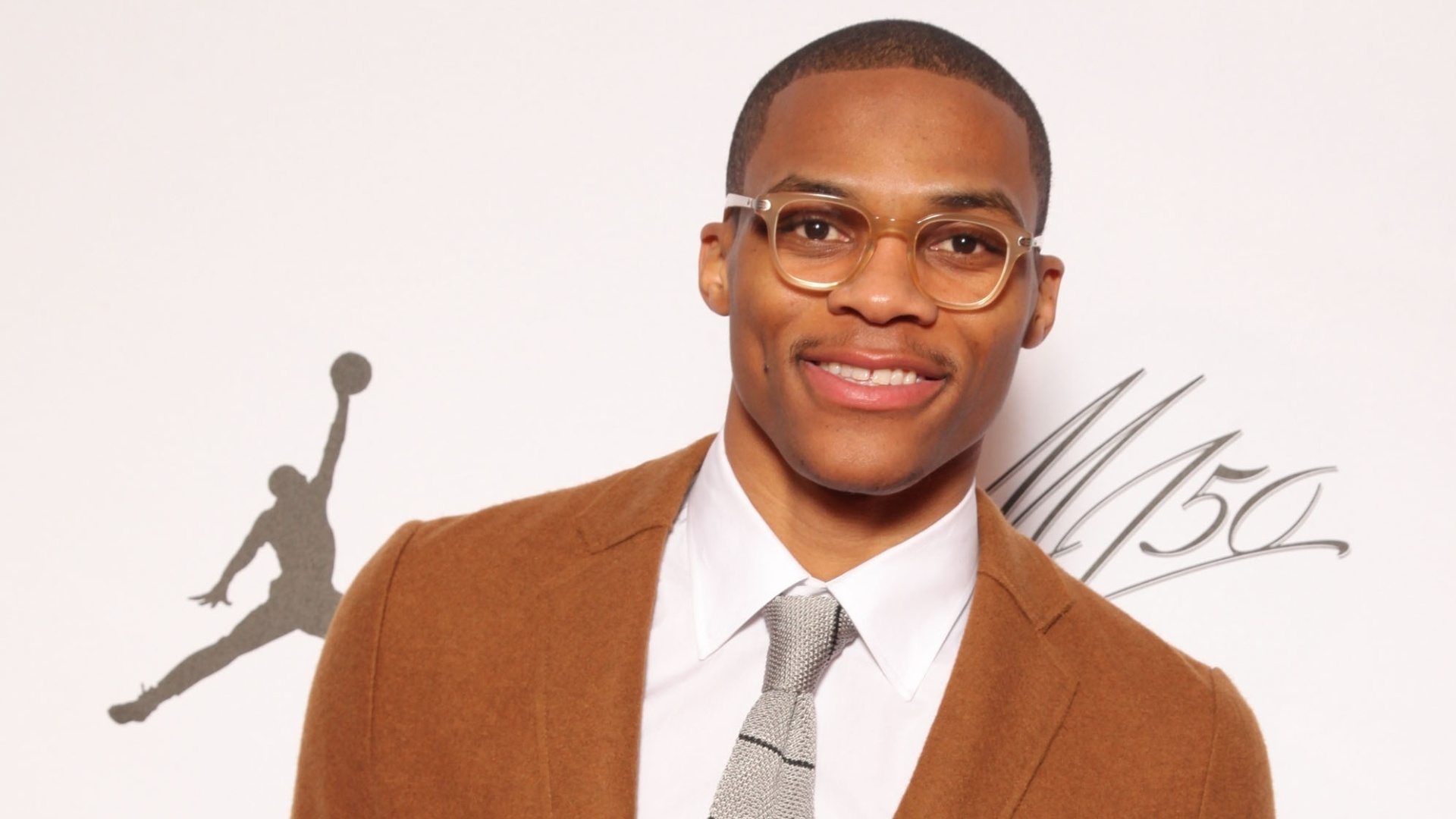 18.fev.2013- Russell Westbrook escolheu uma calça militar, combinada com um terno marrom, gravata cinza e cinto e tênis amarelo para ir à festa de Michael Jordan - Omar Vega/AP Images