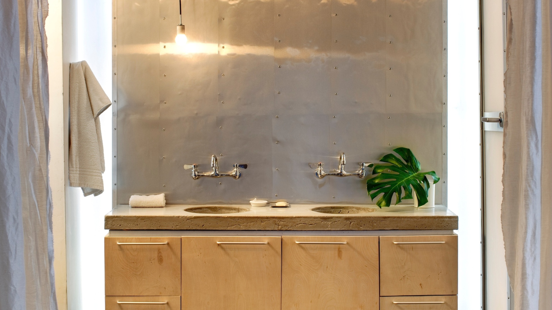 No banheiro, o painel de alumínio reflete a luz da lâmpada simples e a propaga pelo espaço. Destaque para o gabinete de madeira logo abaixo da bancada, com duas cubas, feita de concreto (Imagem do NYT, usar apenas no respectivo material) - Bruce Buck/ The New York Times