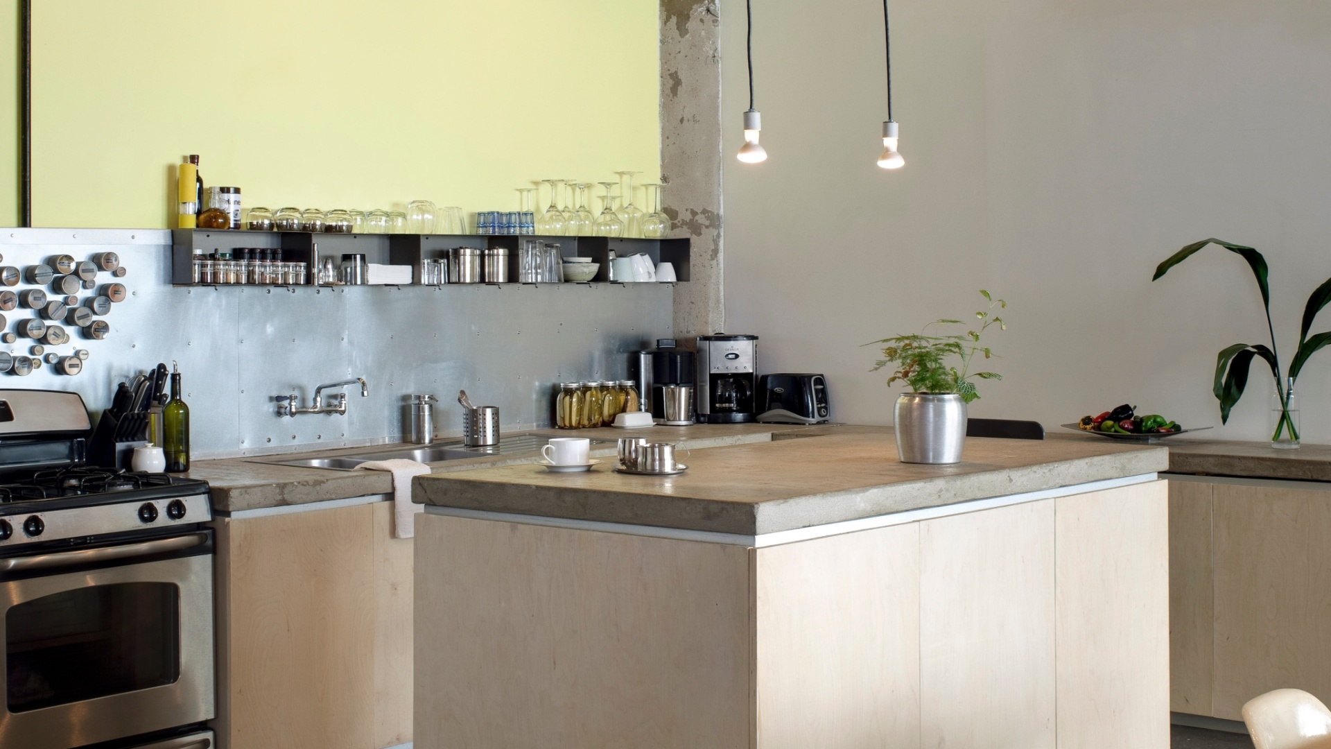 Na cozinha, uma ilha feita com concreto dá apoio ao preparo dos alimentos ou às refeições rápidas. No teto, as lâmpadas pendem em fios e parte do encanamento está aparente, o que dá uma cara industrial ao ambiente (Imagem do NYT, usar apenas no respectivo material) - Bruce Buck/ The New York Times