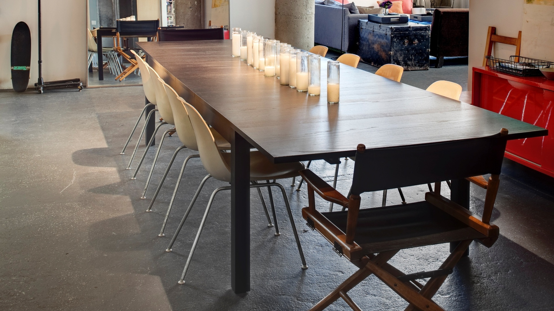 No local destinado à sala de jantar, a mesa ampla é iluminada por refletores com aspecto profissional, há velas sobre o tampo e, à direita, sobre o aparador está um quadro abstrato pintado pelo namorado de  Aubrey Fry - uma das moradoras -, Adam O'Neal (Imagem do NYT, usar apenas no respectivo material) - Bruce Buck/ The New York Times