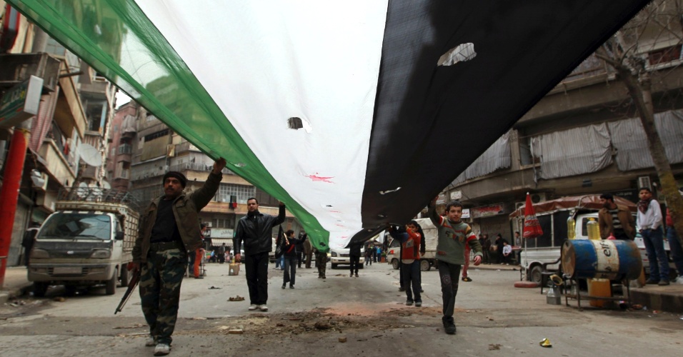 22.fev.2013 - Homens seguram uma bandeira gigante da oposição síria durante protesto contra o presidente Bashar Assad, em Aleppo