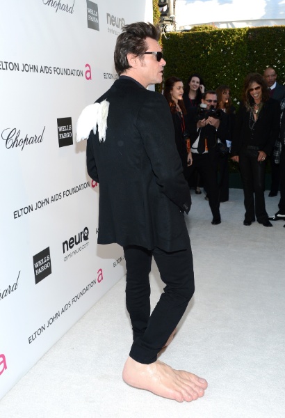 24.fev.2013 - Jim Carrey faz graça na festa de Elton John e aparece com pés gigantes e asas. No fundo, Steven Tyler acha graça do "figurino" do ator