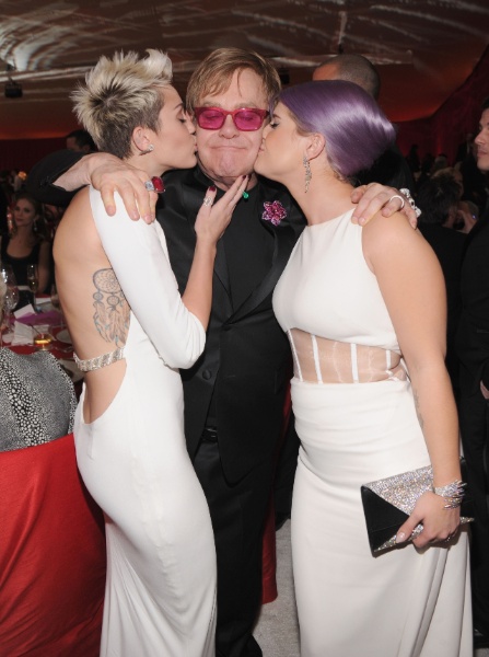 24.fev.2013 - Miley Cyrus e Kelly Osbourne beijam Elton John na festa beneficente que o cantor promoveu em Los Angeles