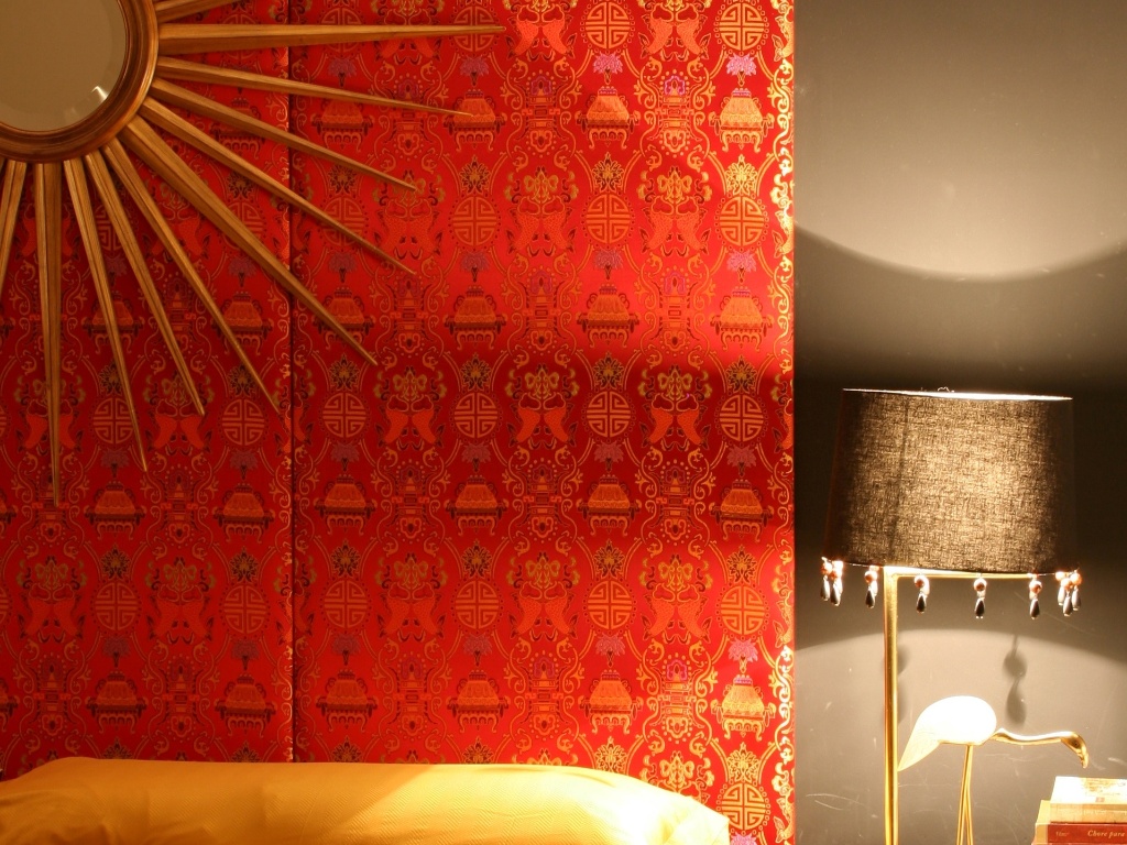 No mesmo projeto de decoração do apartamento em Londrina (PR), assinado pelo arquiteto Guilherme Torres, a decoração do quarto com referências étnicas conta com parte da parede revestida na cor alaranjada intensa, com estampas em tons do amarelo que combinam à peça decorativa, ao centro - Divulgação