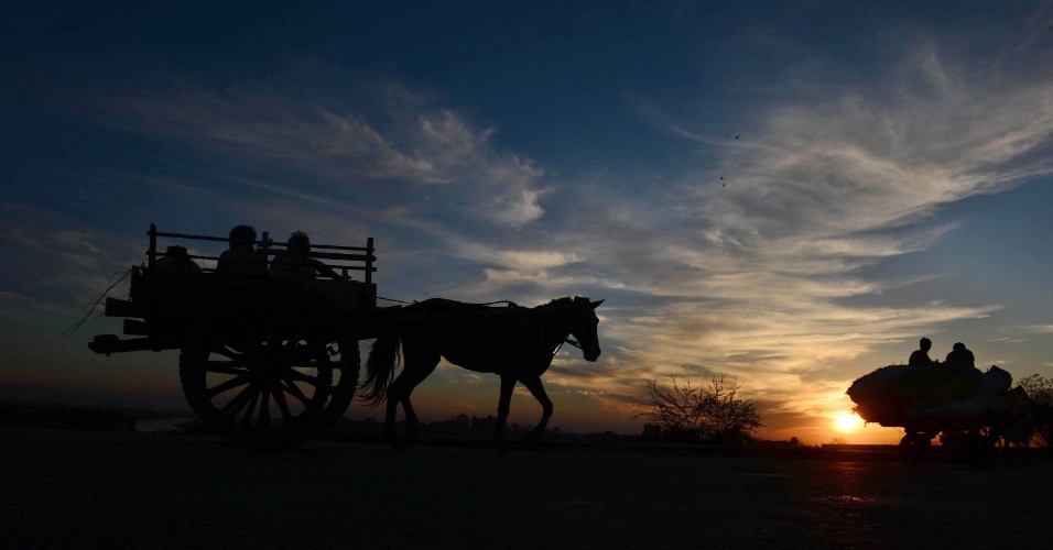 01.mar.2013 - Agricultores viajam para casa em sua carroça puxada por cavalo durante o pôr do sol, em Lahore, no Paquistão