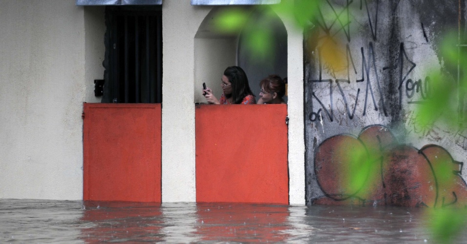 8.mar.2013 - Mulheres se protegem de enxurrada atrás de comportas na rua Venâncio Aires, na Pompeia, em São Paulo (SP), na tarde desta sexta-feira. Ruas da região ficaram alagadas depois que uma forte chuva atingiu a cidade
