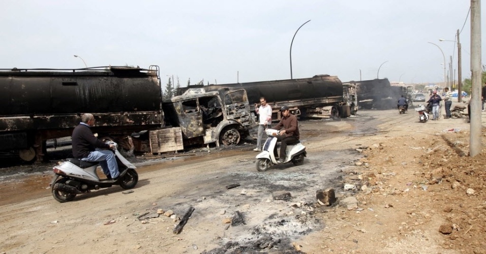 15.mar.2013 - Pessoas passam próximas a caminhões queimados em Trípoli, capital da Líbia, nesta sexta-feira (15). Sete veículos que levavam combustível para a Síria foram interceptado e depredados na noite de quinta-feira (14) por opositores do regime do sírio Bashar Al-Assad, segundo agências de notícias
