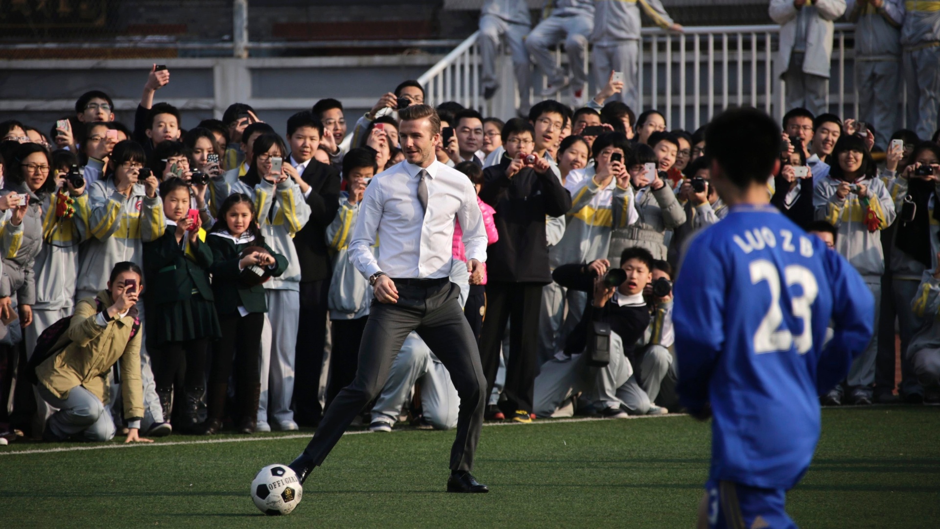 20.mar.2013 - David Beckham nem se importou com os trajes sociais e bateu bola com estudantes na China - Petar Kujundzic/Reuters