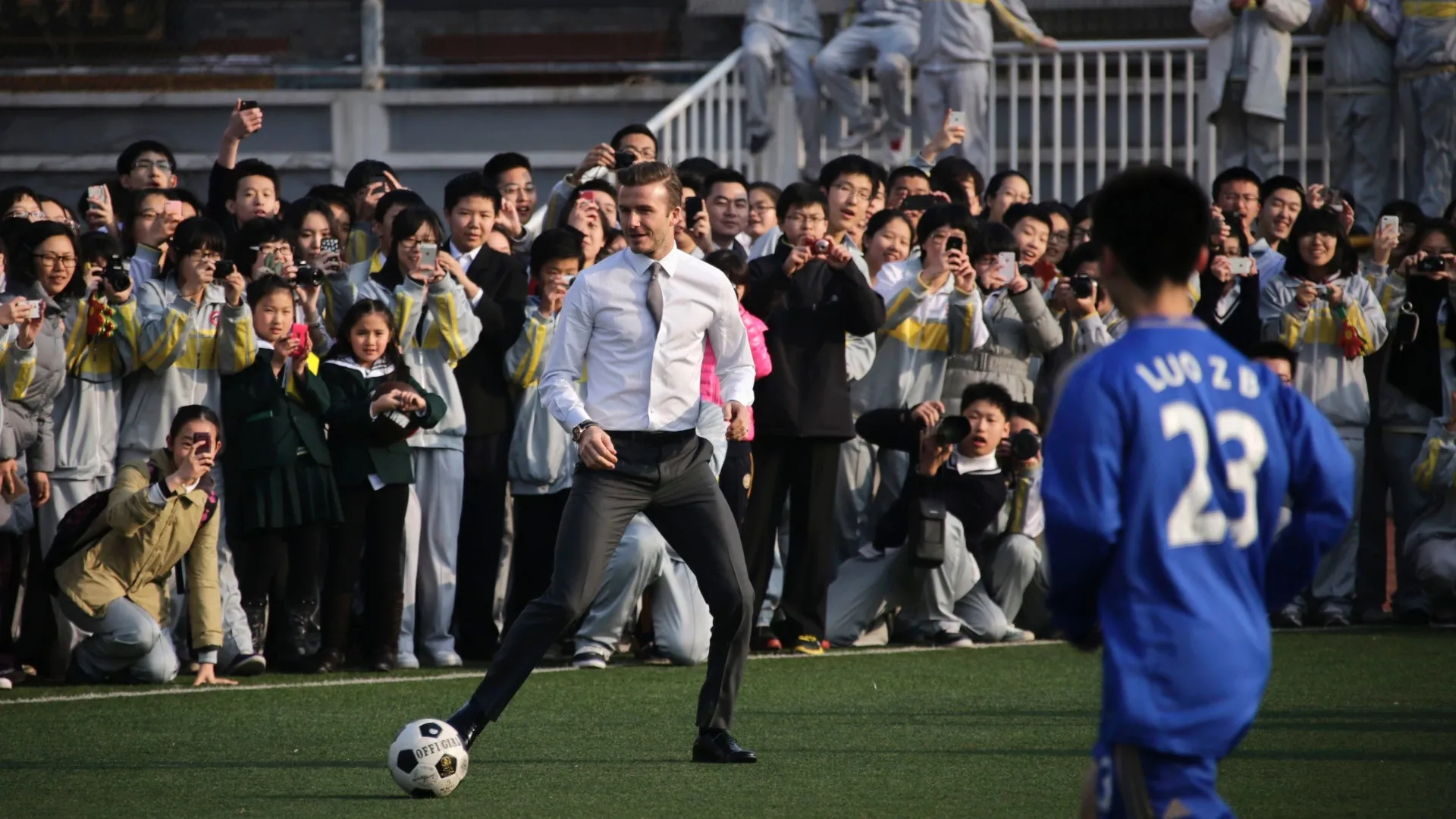 20.mar.2013 - David Beckham nem se importou com os trajes sociais e bateu bola com estudantes na China - Petar Kujundzic/Reuters