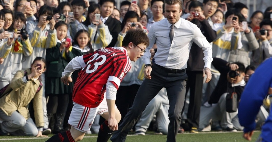 20.mar.2013 - Gravata e sapatos sociais não foram problema para David Beckham jogar bola com estudantes chineses - How Hwee Young/EFE