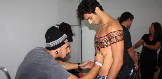 20 mar. 2013 - O tatuador Rafael Firmino faz a pintura corporal do modelo Luis Coppini no camarim do desfile de João Pimenta - Julia Guglielmetti/UOL