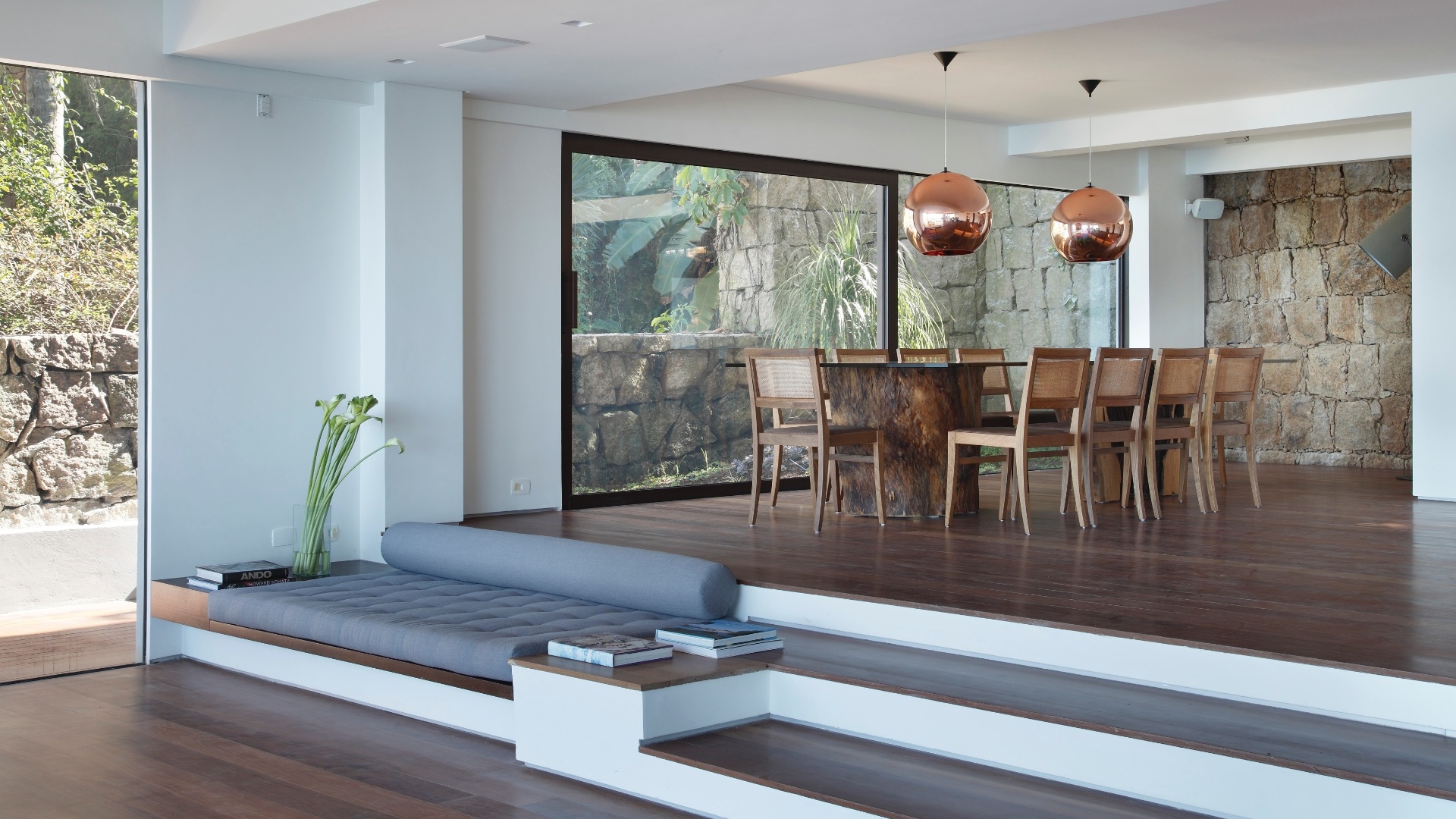 Um pequeno desnível de três degraus separa as salas de jantar e estar que tem sofás de alvenaria e rolos estofados como apoios, possibilitando o "relax" total e a visualização completa da paisagem. A Casa do Joá tem projeto de reforma do escritório House in Rio e fica na Praia da Joatinga, Rio de Janeiro - Denilson Machado/ MCA Studio/ Divulgação