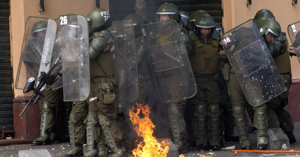 11.abr.2013 - Policiais se protegem durante manifestação que reuniu milhares de chilenos nesta quinta-feira (11). A marcha percorreu as ruas de Santiago para exigir uma educação pública gratuita e de melhor qualidade