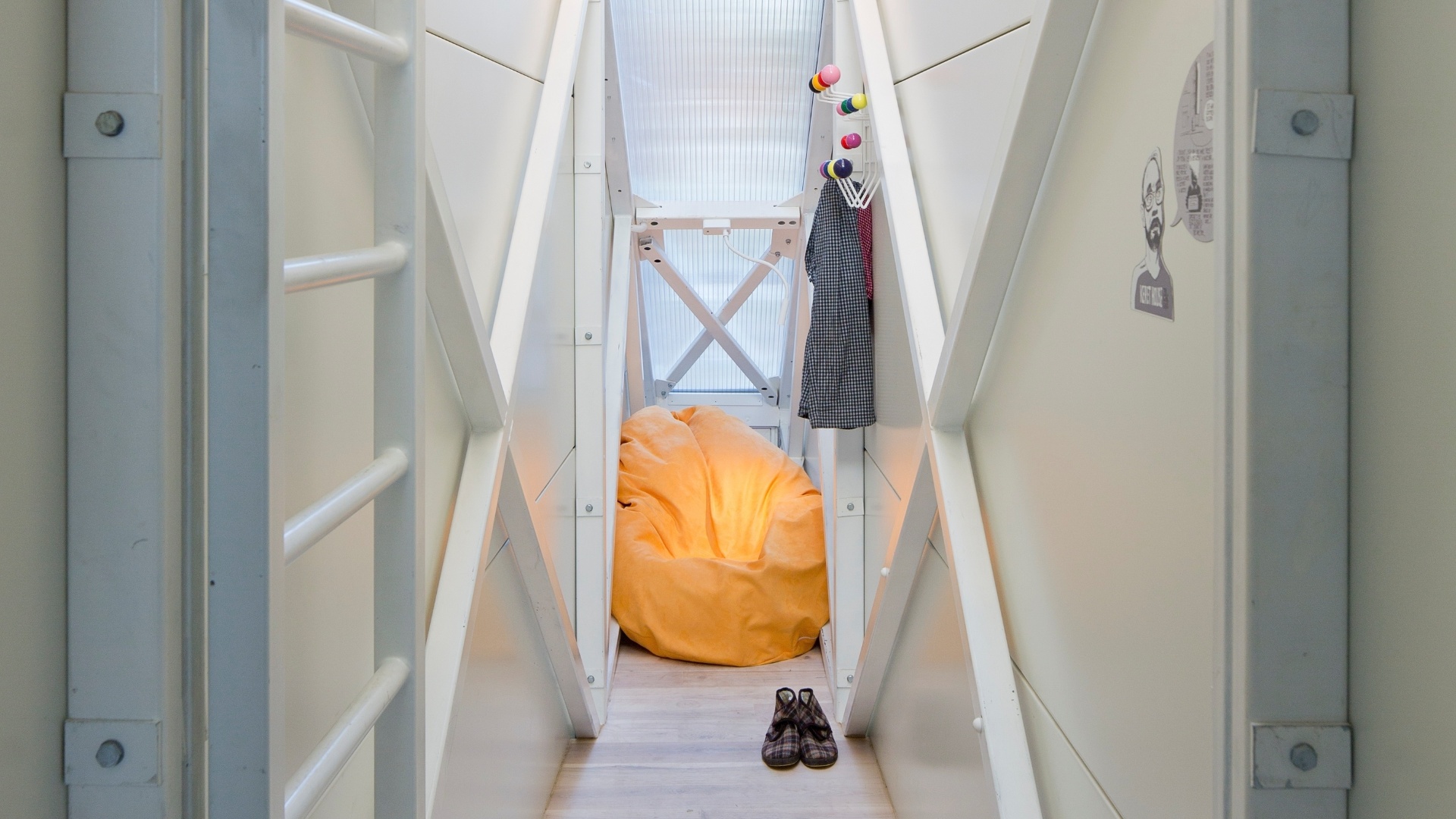 Na sala de estar da Casa Keret, em Varsóvia, Polônia, à frente, o alcapão que leva ao andar inferior e ao fundo, o grande pufe na cor alaranjada se contrasta com as paredes brancas.  A estreita residência localizada "espremida" entre dois prédios foi projetada pelo arquiteto polonês, Jakub Szczesny - Andrea Meichsner/The New York Times