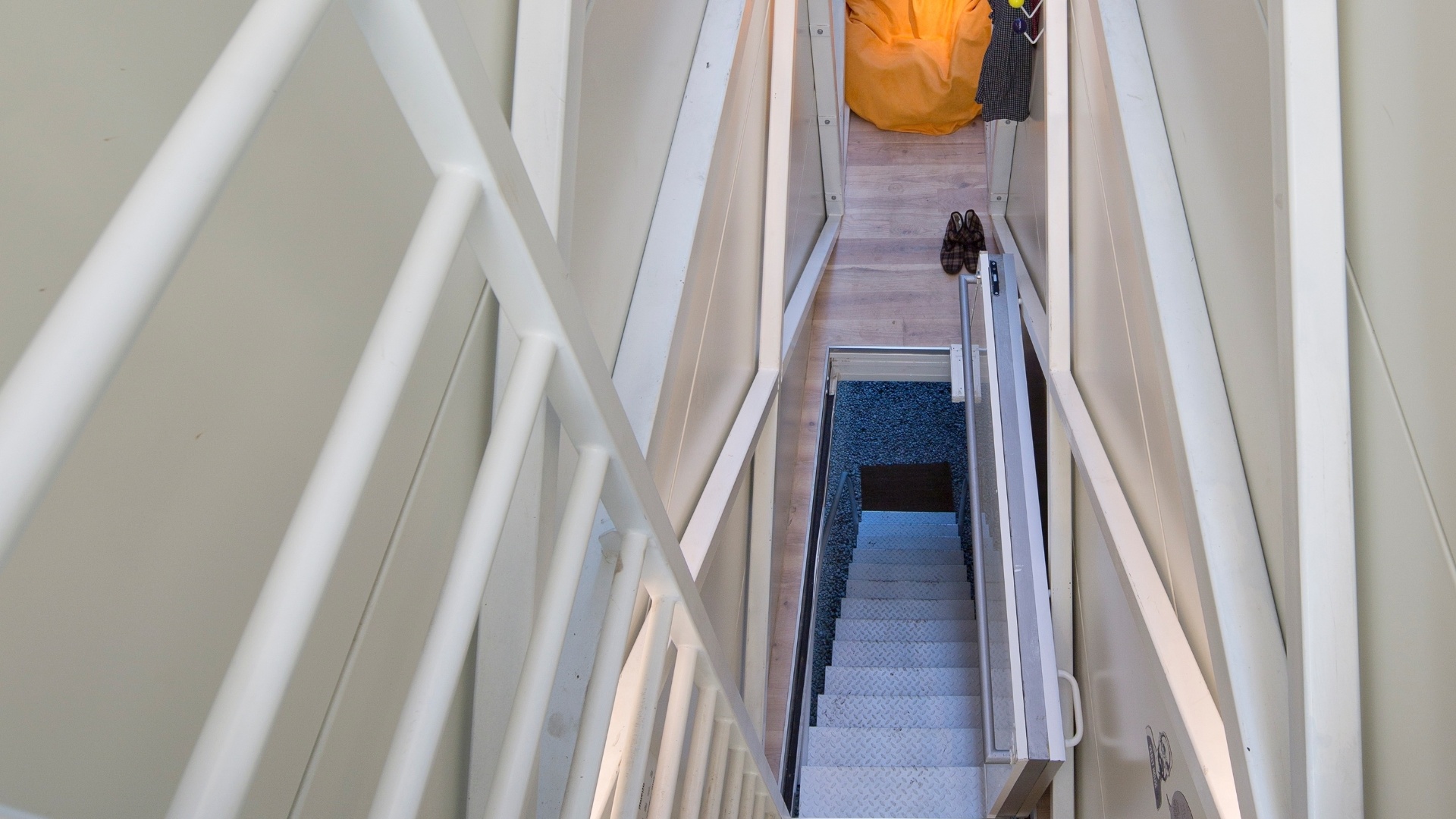 Na sala de estar da Casa Keret, em Varsóvia, Polônia, à frente, o alcapão que leva ao andar inferior e ao fundo, o grande pufe na cor alaranjada se contrasta com as paredes brancas.  A estreita residência localizada "espremida" entre dois prédios foi projetada pelo arquiteto polonês, Jakub Szczesny - Andrea Meichsner/The New York Times