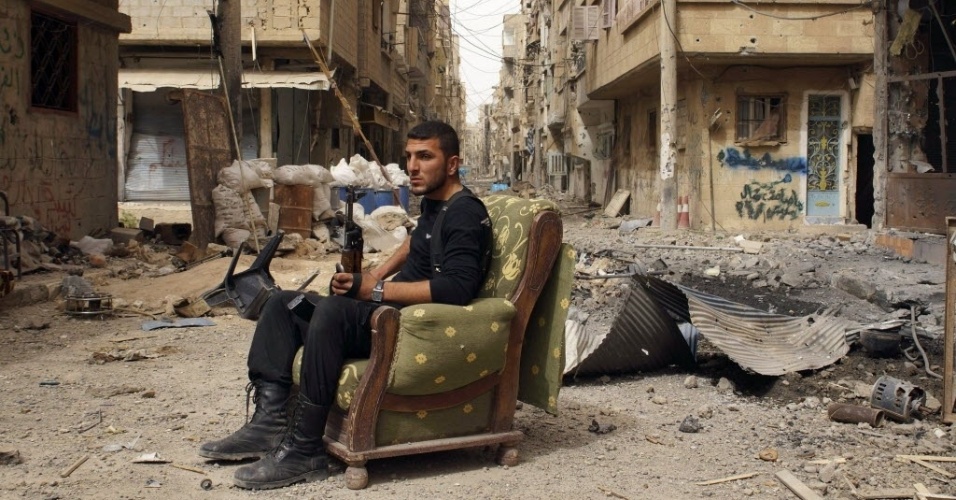 2.abr.2013 - Combatente do Exército Livre da Síria segura arma sentado em sofá no meio de rua destruída em Deir al-Zor, na Síria