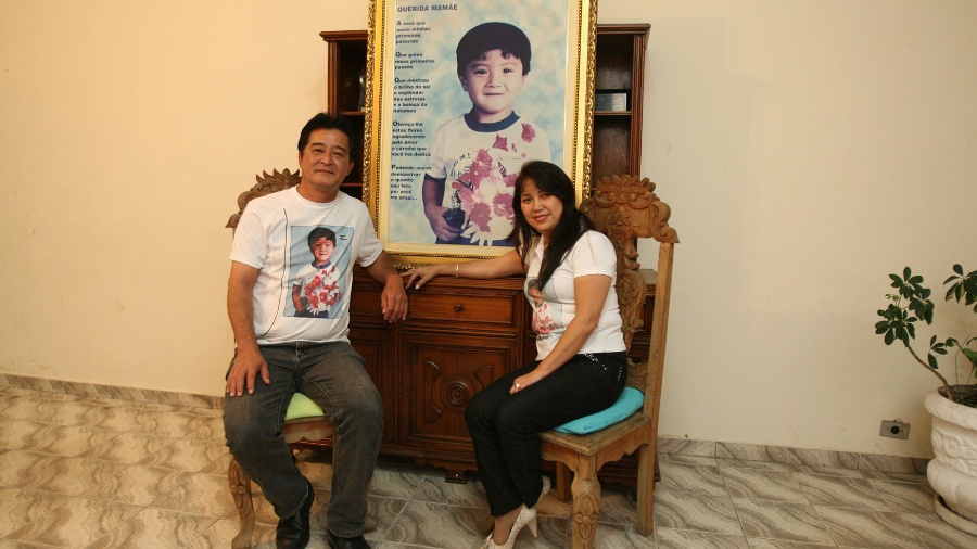 O casal Masataka Ota e Iolanda Keiko Ota em frente ao quadro que homenageia o filho Ives Ota, assassinado em 30 de agosto de 1997 - Silva Junior/Folhapress