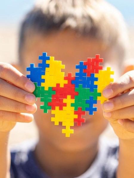 Criança segura coração com as cores do símbolo do Transtorno do Espectro Autista - iStock