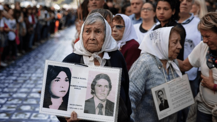 24.mar.2019 - Membros da organização de Direitos Humanos "Madres de Plaza de Mayo" ao lado de uma grande faixa com retratos de pessoas desaparecidas na ditadura militar de 1976-1983