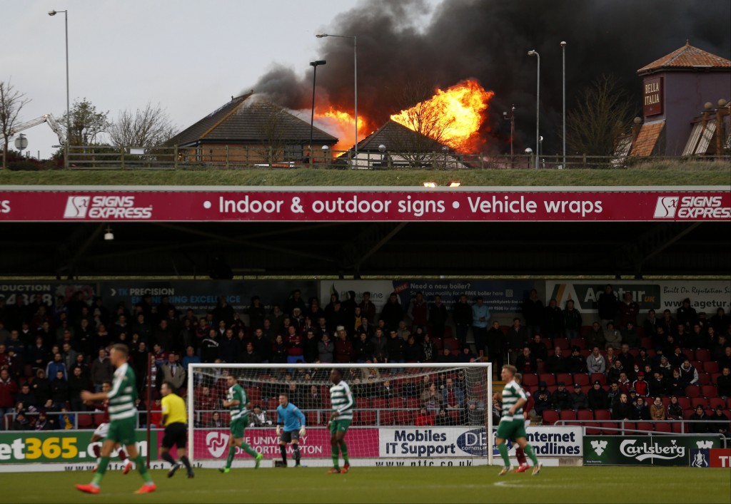 Fire rages at the near by Sixfields Tavern as play continues during the FA Cup second round match between Northampton and Norwich Victoria at Sixfields Stadium, Northampton, central England, Saturday Dec. 5, 2015. (Paul Harding/PA via AP) UNITED KINGDOM OUT NO SALES NO ARCHIVE ORG XMIT: LON836