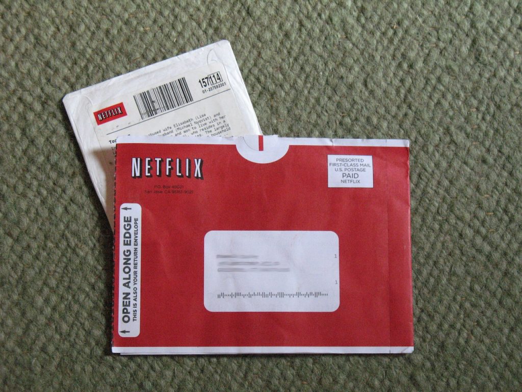 Overhead close-up view of a Netflix movie rental envelope and DVD sleeve lying on a rug.