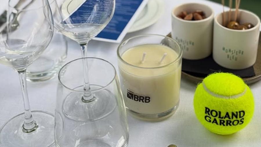 Mesa com bolas de tênis em Roland Garros e uma vela com o logo do BRB Mesa com bolas de tênis em Roland Garros e uma vela com o logo do BRB