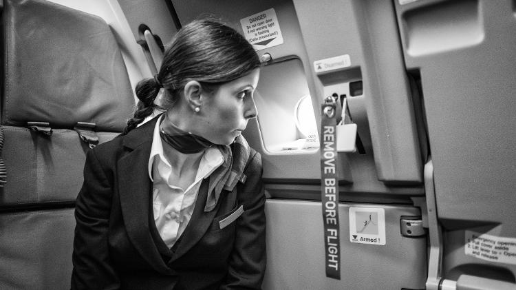 Comissária de bordo observa exterior do avião por meio de janela instalada na porta da aeronave