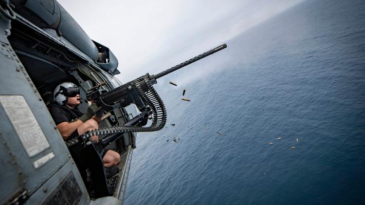Militar dispara uma metralhadora M3 calibre .50 a bordo de um helicóptero Black Hawk Militar dispara uma metralhadora M3 calibre .50 a bordo de um helicóptero Black Hawk