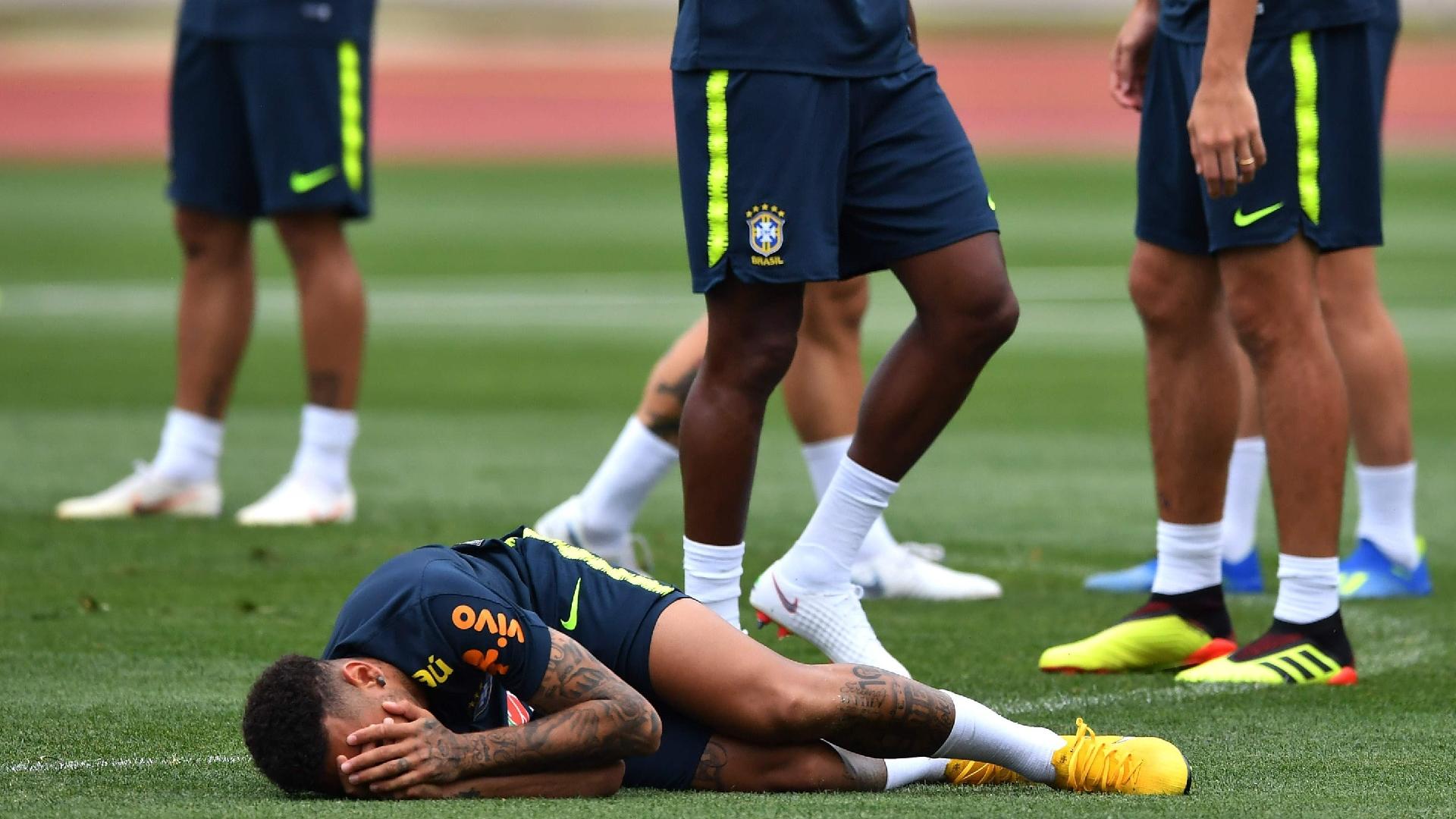 Neymar rola do gramado enquanto companheiros riem em treino do Brasil em Sochi