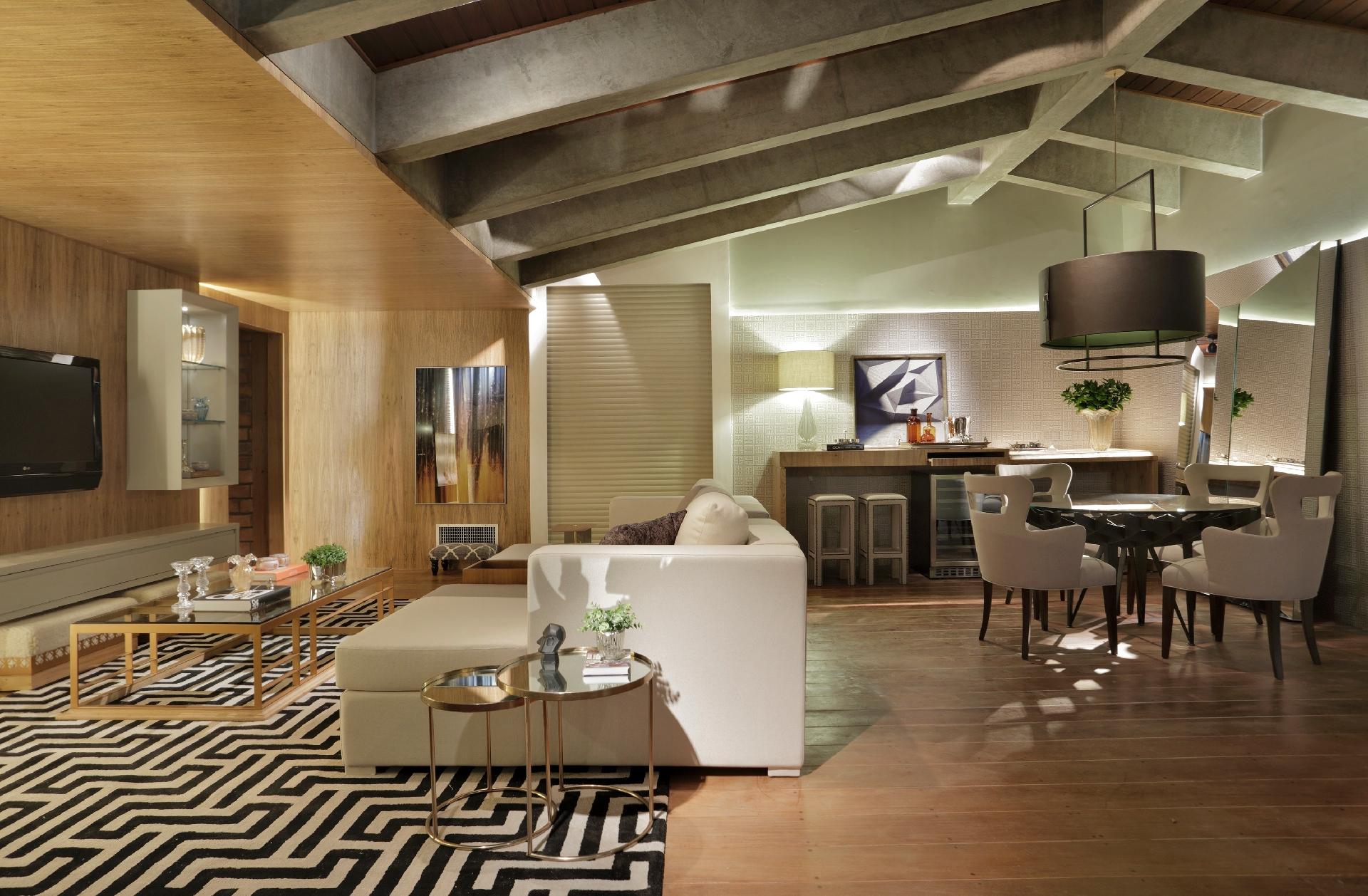 Casa Cor MS - 2016: na Sala de Convívio, criada por Annelise Giordano e Gelise Almeida, leveza e rusticidade se encontram. A madeira clara reveste boa parte da parede (à esq.) e um primeiro nível do teto. Por sua vez, a superfície mais ao fundo tem acabamento sutil, evidenciado pela iluminação indireta e se alinha à ambientação refinada, contrastando com o teto bruto de concreto - Denilson Machado/Divulgação