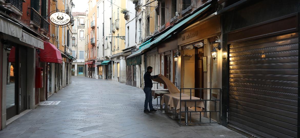 Garçom arruma a mesa de restaurante em rua vazia em meio ao surto do coronavírus em Veneza, na Itália - Marco Di Lauro/Getty Images
