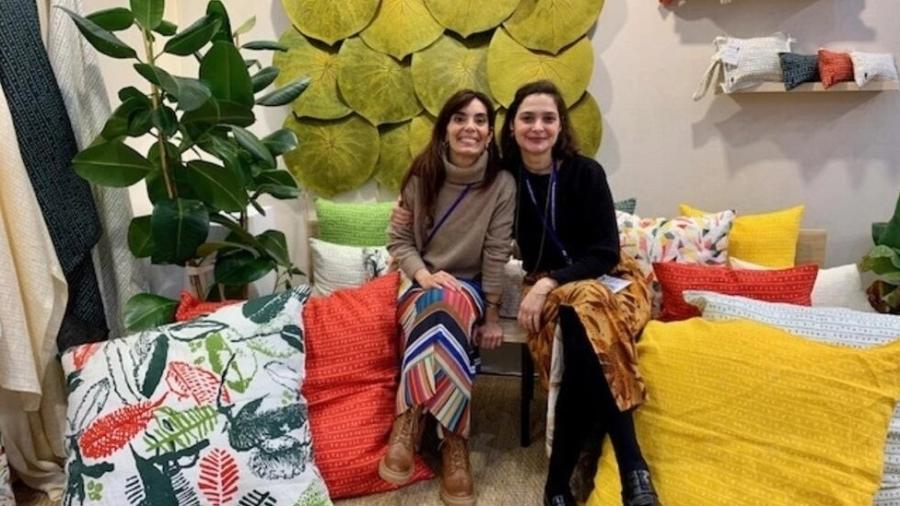 As sócias Ana Lozon (à esquerda) e Bianca Motta, da marca Sabiá, em stand no salão Maison&Objet, em Paris. Ao fundo, as folhas amazônicas de borracha natural, que são vendidas como jogos americanos  - Paloma Varón/RFI