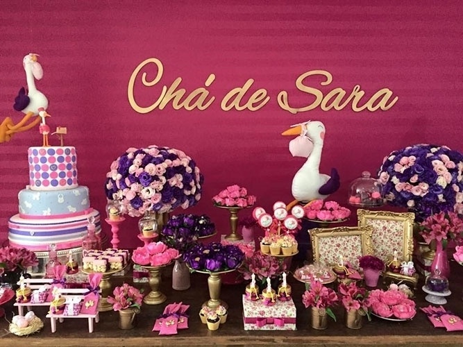 O bolo cenográfico do chá de fraldas, com três andares, é da Aldery Rocha (instagram.com/alderyrocha). No topo, cegonha e caixa de correio de biscuit.  Macarons pink (frutas vermelhas) e os roxos (baunilha), em cúpula de vidro, são da Pantone Macarons (instagram.com/pantonemacarons) - Divulgação