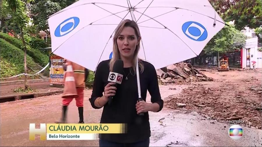 Repórter Cláudia Mourão, sem a menor cerimônia, com microfone numa mão e guarda-chuva na outra - Imagem
