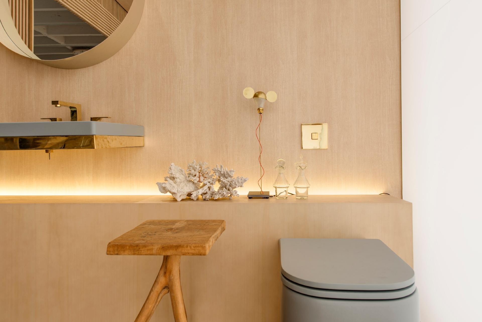 A bancada do banheiro criado pelo escritório Yamagata, na edição paulistana da Casa Cor, tem iluminação indireta e posterior, que destaca os objetos de decoração, o acabamento da parede e o lavarório cinza e dourado da Deca. Entre as poucas peças ali dispostas, a luminária do designer alemão Ingo Maurer, batizada de 'I Ricchi Poveri - Toto', chama a atenção - Katia Kuwabara/UOL