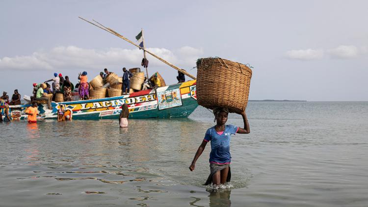 Mulher carrega cesta de mercadorias após descarregá-las de um barco que levava suprimentos para a Ilha Nyangai Mulher carrega cesta de mercadorias após descarregá-las de um barco que levava suprimentos para a Ilha Nyangai