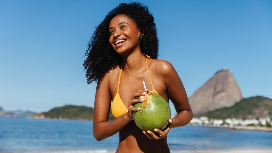 Mulher na praia consumindo água de coco