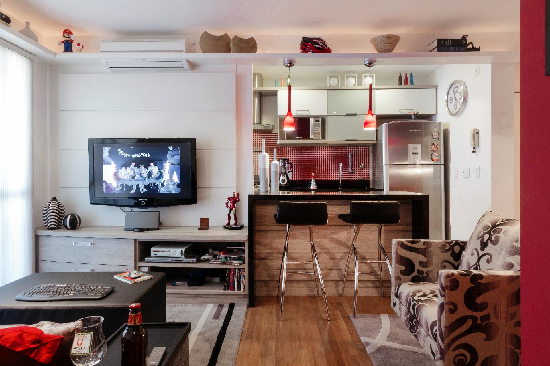 A prateleira rente ao teto contorna toda a sala. O objetivo da arquiteta Emilia Garcia era que, com ela, o morador pudesse expor seus objetos de decoração mais queridos. Para valorizá-los ainda mais, foi instalada uma fita LED embutida ao fundo das ripas. Uma das prateleiras ainda serve de base para dois pendentes sobre a bancada - Divulgação