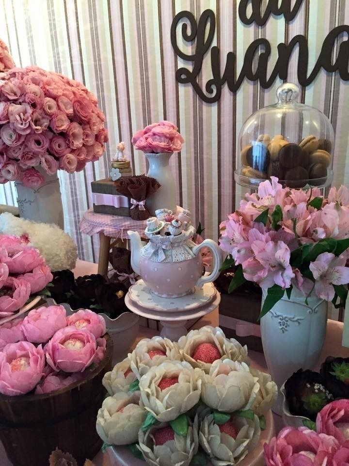 Bule decorado sobre prato laqueado na cor rosa bebê. Ao lado, vaso de louça branco com astromélias naturais. Dentro da cúpula de vidro com pé, macarons de chocolate e limão da Pantone Macarons (instagram.com/pantonemacarons) - Divulgação