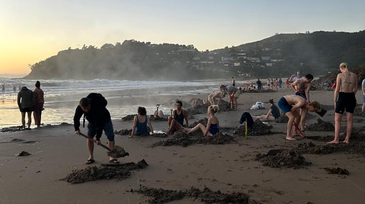 Pessoas cavam para encontrar águas termais em plena areia de Hot Water Beach Pessoas cavam para encontrar águas termais em plena areia de Hot Water Beach