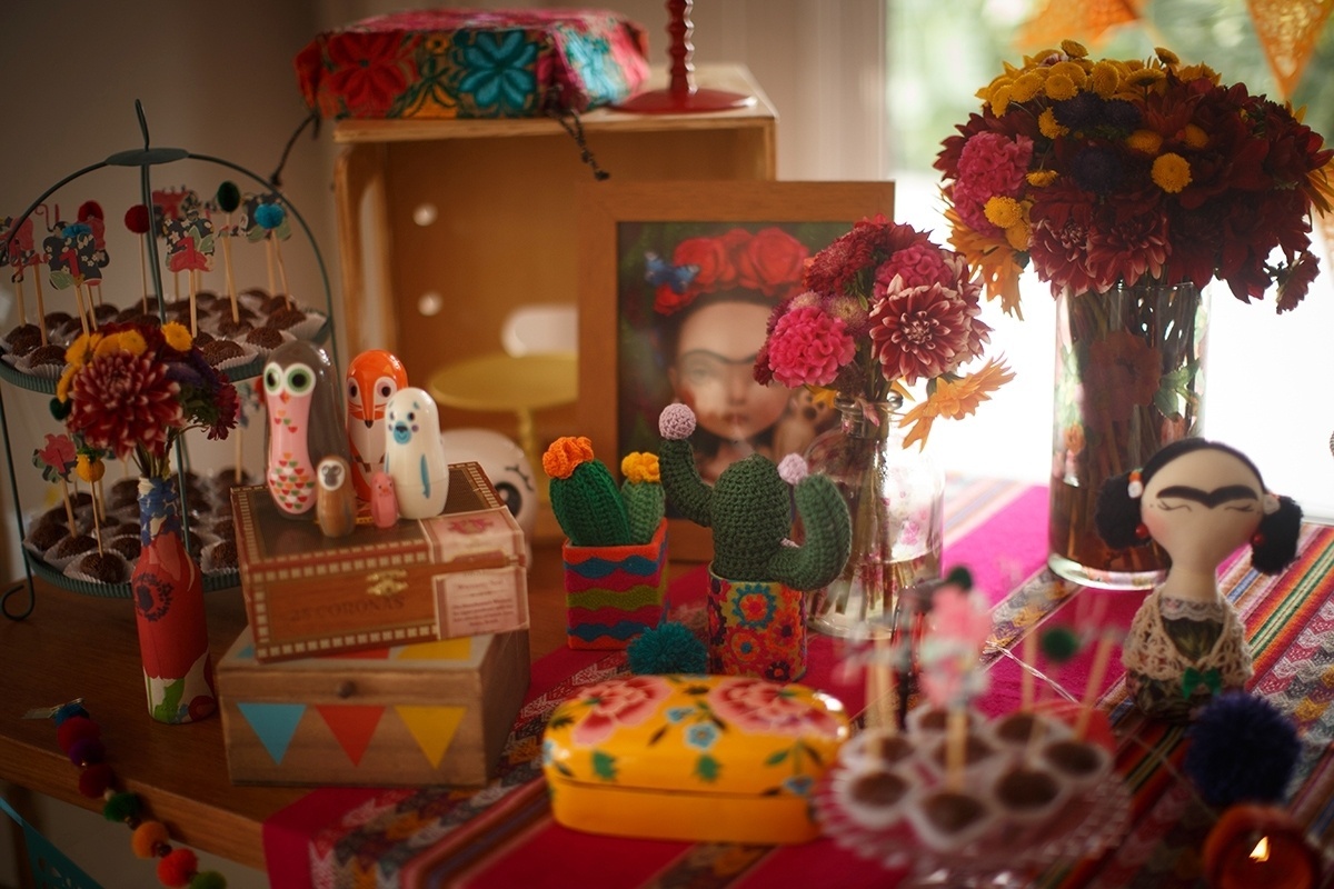 Detalhes da decoração da mesa principal da festa de um ano inspirada em Frida Kahlo. Caixinhas e enfeites coloridos, artesanato típico do México, e imagens da artista ao lado de vasos de flores do campo - Ilana Lichtenstein/Divulgação