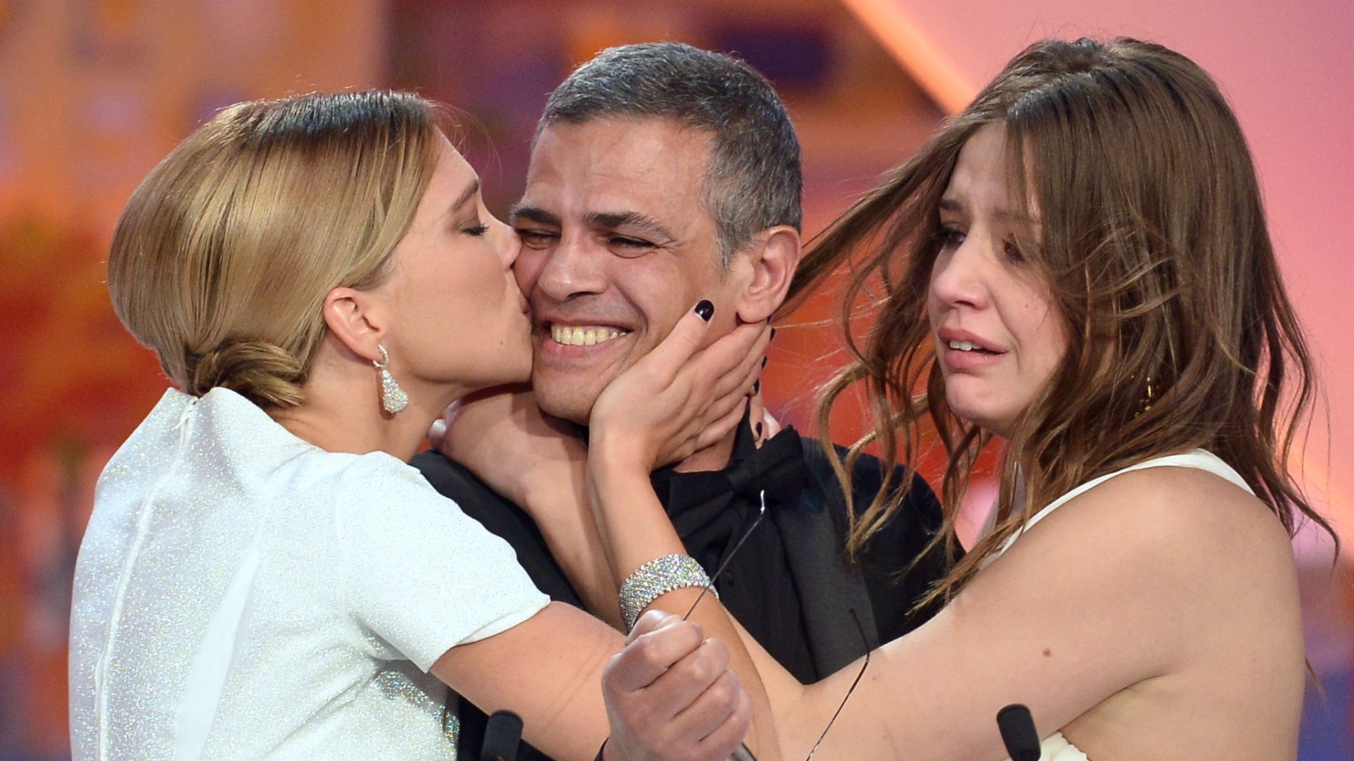 26.mai.2013 - As atrizes francesas Lea Seydoux (à esq) e Adele Exarchopoulos abraçam o diretor franco-tunísio Abdellatif Kechiche enquanto ele recebe a Palma de Ouro pelo filme "La Vie d'Adele", durante o encerramento do Festival de Cannes - Alberto Pizzoli/AFP Photo
