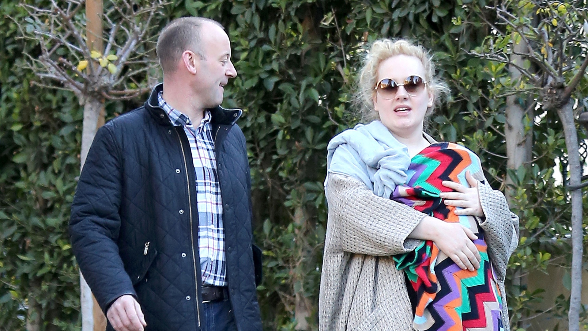 De calça legging, sapatilhas e casacão, Adele passeia com seu filho no colo em look confortável e prático para as mães. Mulheres acima do peso também podem usar legging, contanto que o bumbum fique coberto pela blusa, vestido ou casaco - Grosby Group