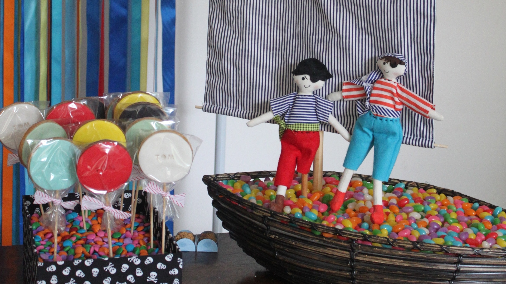 Para decorar a mesa central da festa Pirata, foi colocada uma cesta em forma de casco lotada de doces (conhecidos como delicados). Para completar o barco, uma vela e dois personagens enfeitam a cesta. A mesma ideia foi usada na caixinha decorada ao lado, que traz pirulitos espetados - Divulgação