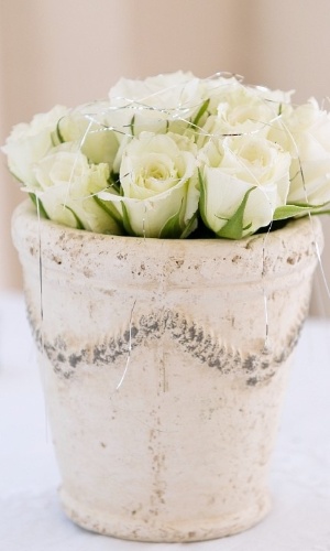 Centro de mesa com rosas brancas em vaso rústico. Vasos de plantas antigos, com a pintura gasta, ficam lindos com rosas dentro deles. A mistura proporciona um equilíbrio entre o delicado e o rústico e combina com casamentos ao ar livre