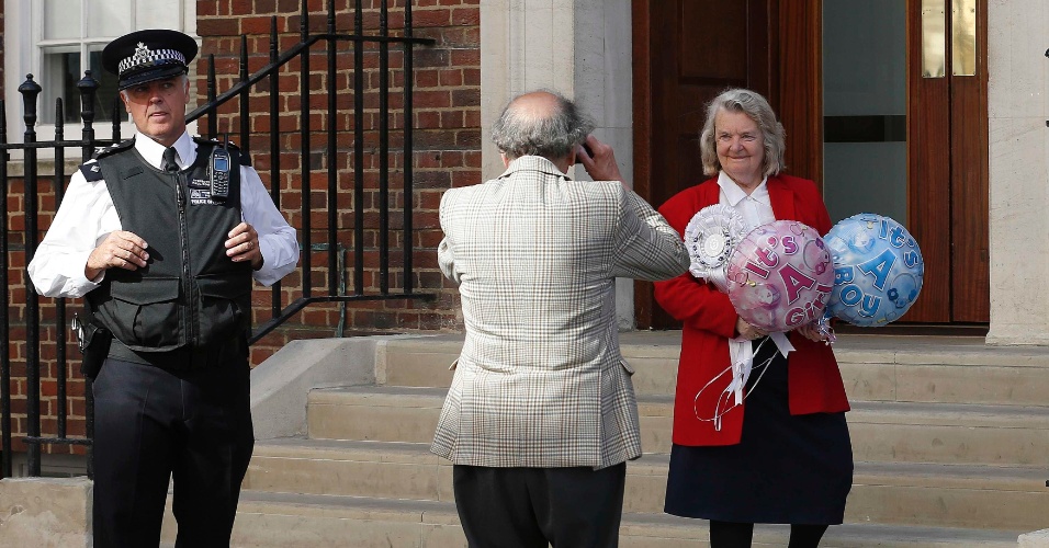 15.jul.2013 - Fã da família real, Magraret Tyler posa para foto com balões onde se lê "é uma menina" e "é um menino". Ela estava em frente à ala Lindo do hospital St. Mary, onde nascerá o primeiro bebê de Kate Middleton e do Príncipe William. A Duquesa de Cambridge deve dar à luz ainda neste mês