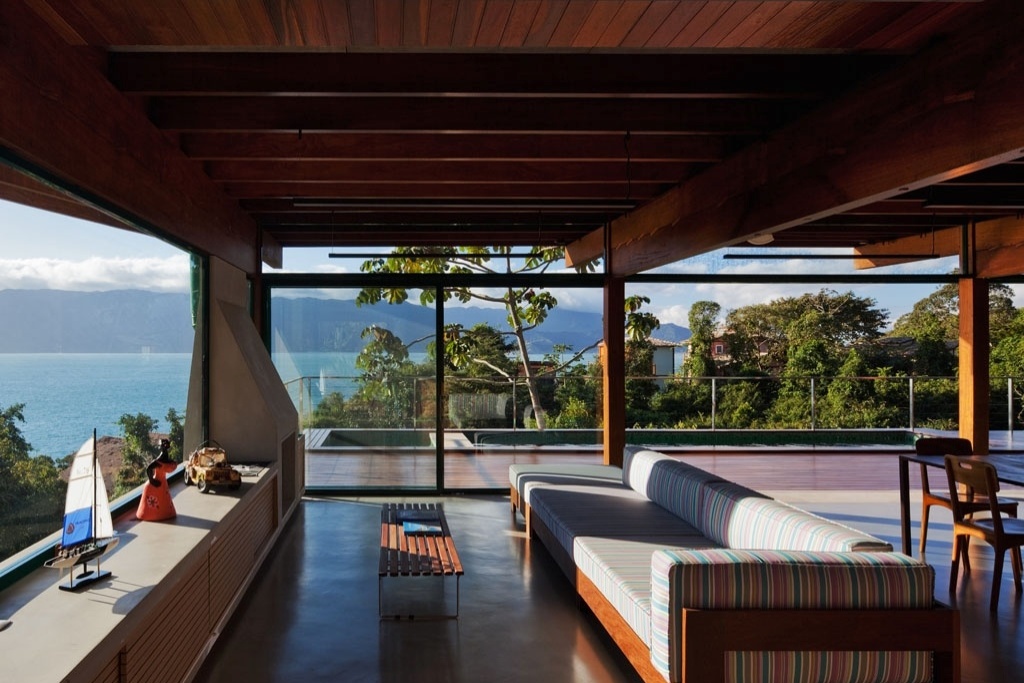 A área de convívio está agrupada no térreo, de onde - graças ao fechamento em vidro - é possível desfrutar da magnífica paisagem formada por céu, mar e montanhas. Na Casa Embaúba, projetada pela arquiteta Flavia Cancian, o living conta com lareira, piso em cimento polimérico e vigas de cumaru e está diretamente ligado ao deck com piscina, próxima à mata de preservação permanente - Nelson Kon/ UOL