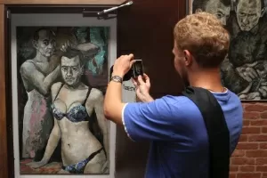 Visitante fotografa a pintura "Travesti", de Konstantin Altunin, em uma exposição no "Museu do Poder", em São Petersburgo (Rússia). A obra representa o presidente Vladimir Putin e o primeiro-ministro Dimitri Medvedev vestidos de mulher - Stringer/Reuters