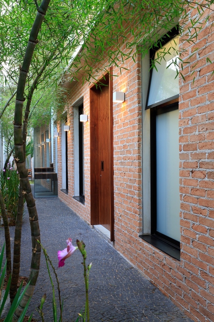 O acesso social à residência se dá pela face lateral, onde estão as aberturas para o living e a porta principal em nogueira. O piso, composto por pedras portuguesas pretas, forma interessante contraste com os tijolos de demolição que dão estrutura à rústica parede. A Casa Urbana foi projetada pela arquiteta Paula Bittar - Sergio Scripilliti/ Divulgação