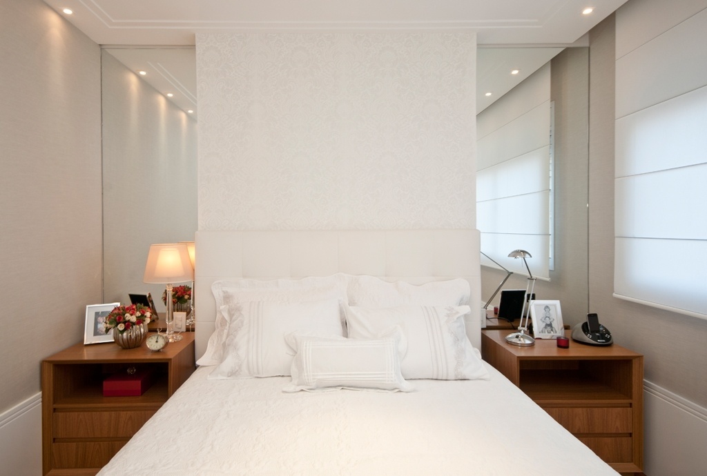Na projeto do escritório AHGA Arquitetura o destaque fica por conta da parede atrás da cama. Nela, a cabeceira estofada se apoia sobre o papel de parede da Petit Décor decorado com arabescos em tons "off-white". Nas laterais, as faixas de espelho distribuem a luz e dão a sensação de amplitude ao ambiente. Os criados-mudos em tom mais quente, de madeira, dão mais aconchego ao quarto - Henry Lopes/ Divulgação